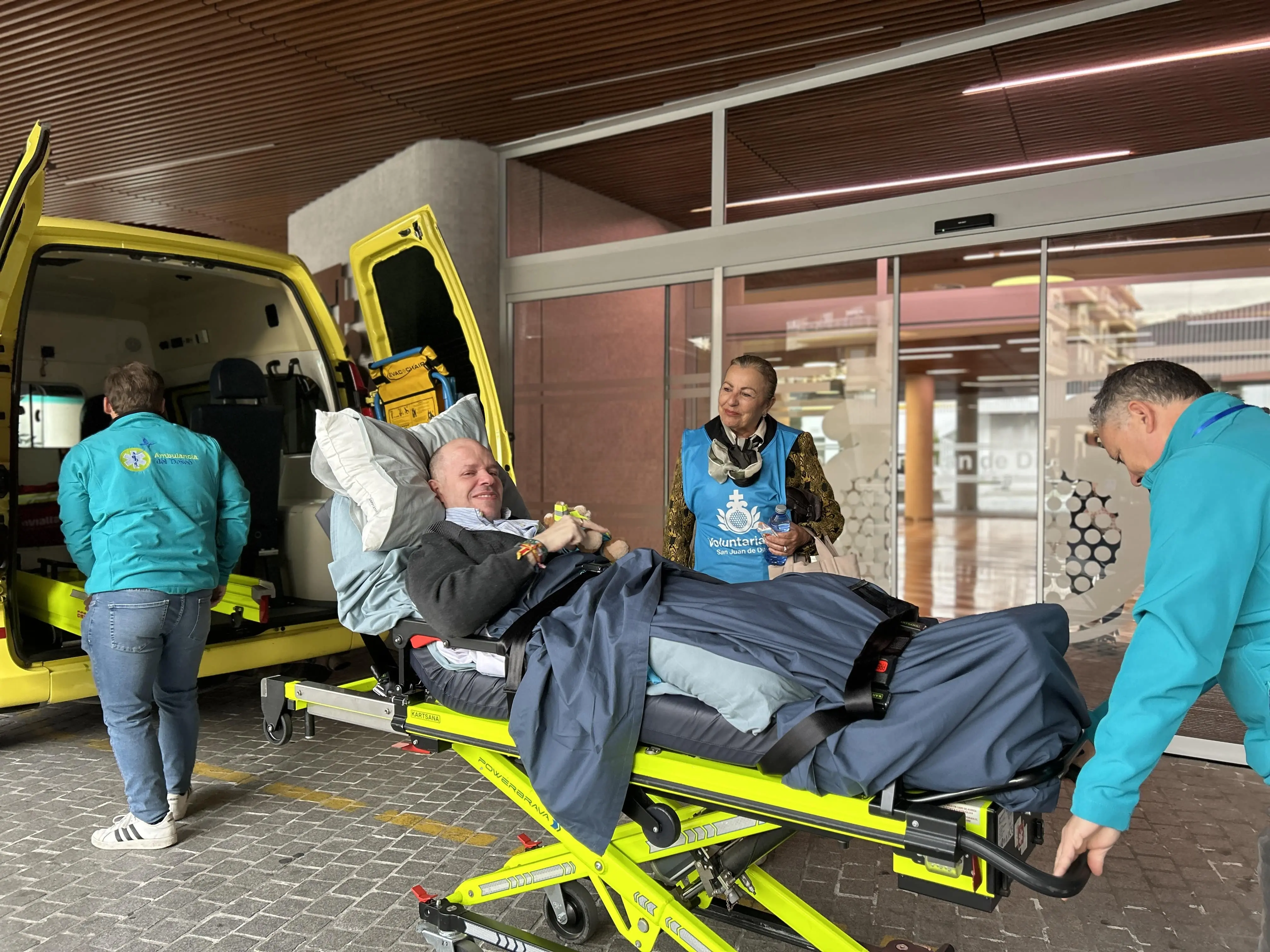 Sanitarios de la Ambulancia del Deseo preparan al paciente para trasladarlo a la Basílica del Gran Poder junto a una voluntaria de San Juan de Dios